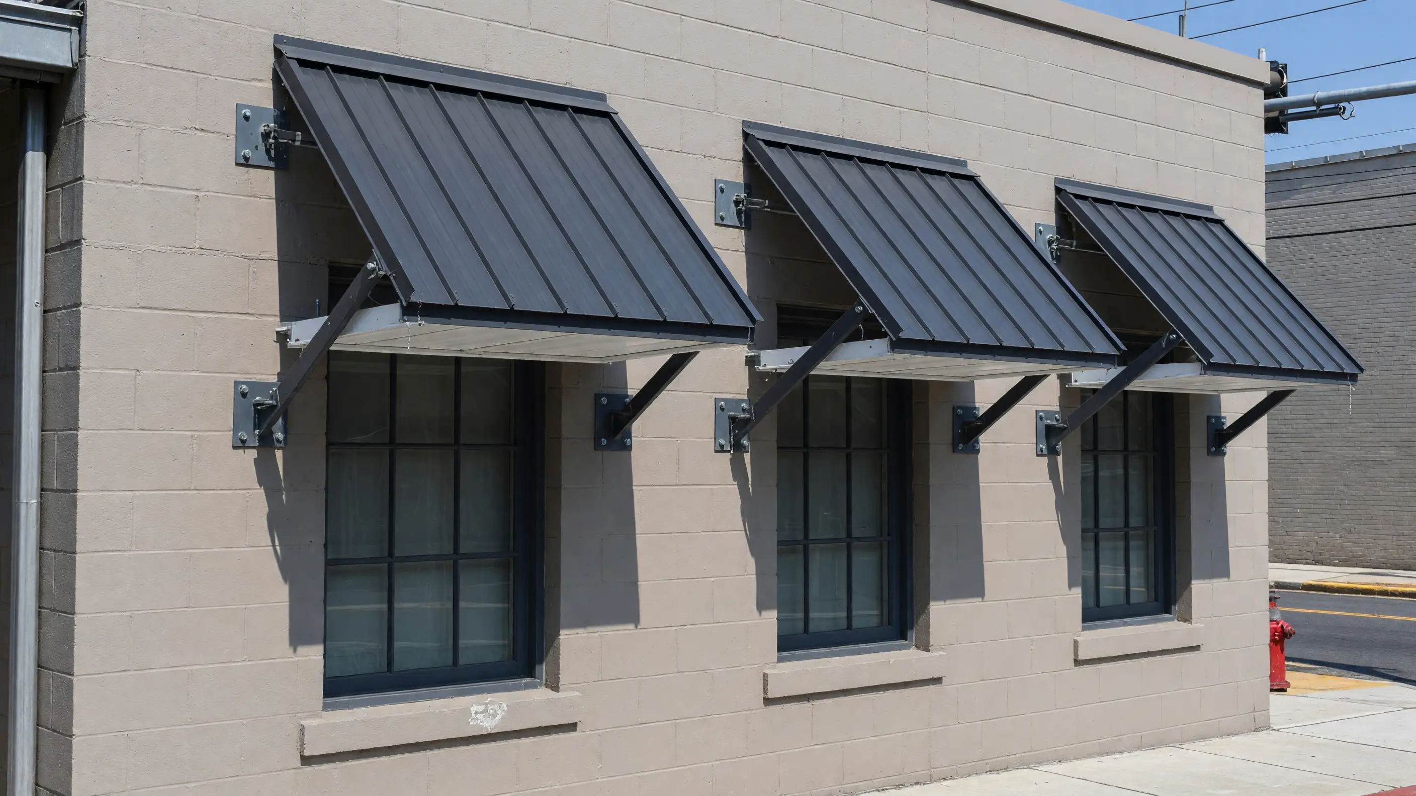 Three matching steel window awnings on a light masonry facade