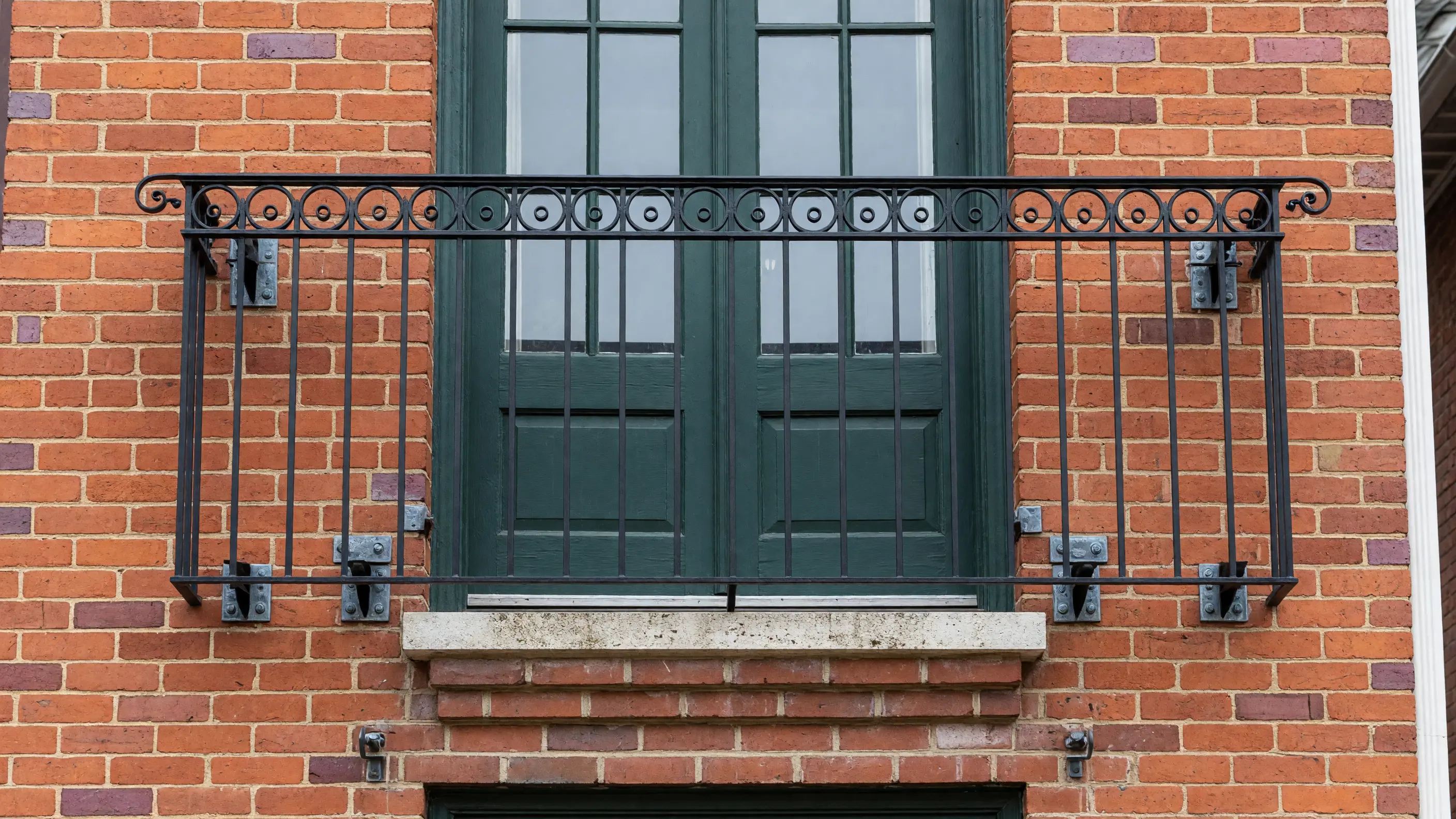Traditional steel Juliet balcony railing mounted across French doors on a warm brick facade