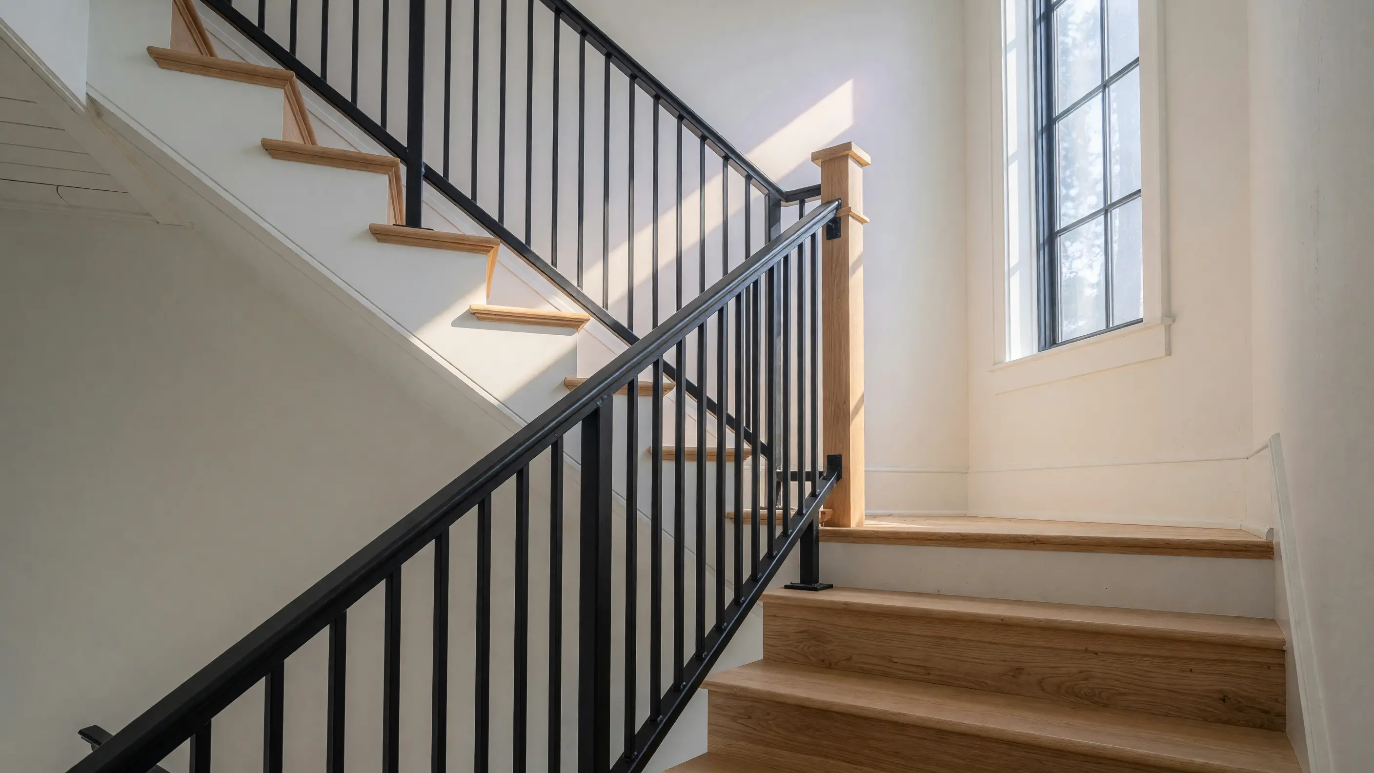 Matte black flat-bar steel railing climbing a white-oak staircase in a renovated Charlotte home